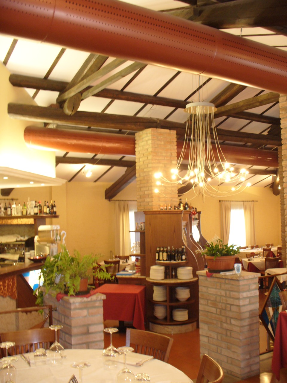 Vista del ristorante con canali microforati colorati, travi in legno e pilastri in mattoni